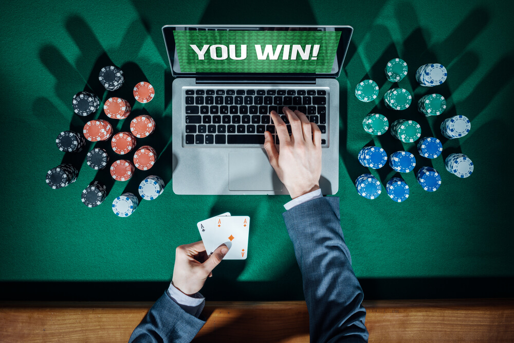 Online player's hands with laptop and stack of chips all around on green table top view